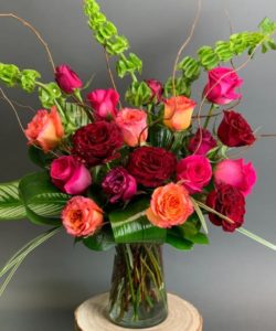 vase includes a mix of vibrant colored roses arranged with tropical greens and modern flair