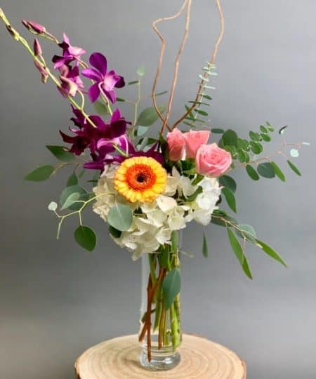A modern bud vase, with hydrangea and mini roses, accented with orchids and a gerbera daisy.